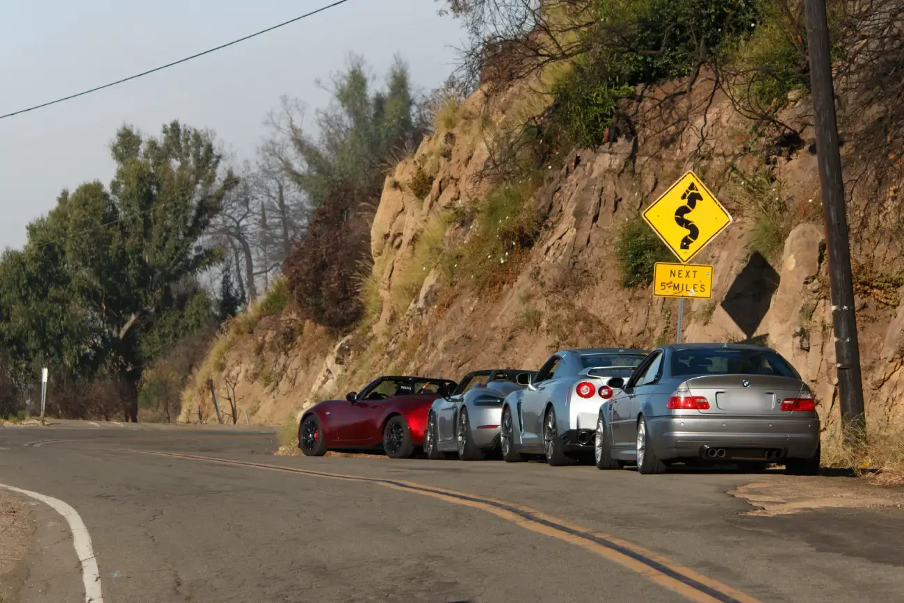 Cars pulled over on a Malibu canyon road with a curves-ahead sign